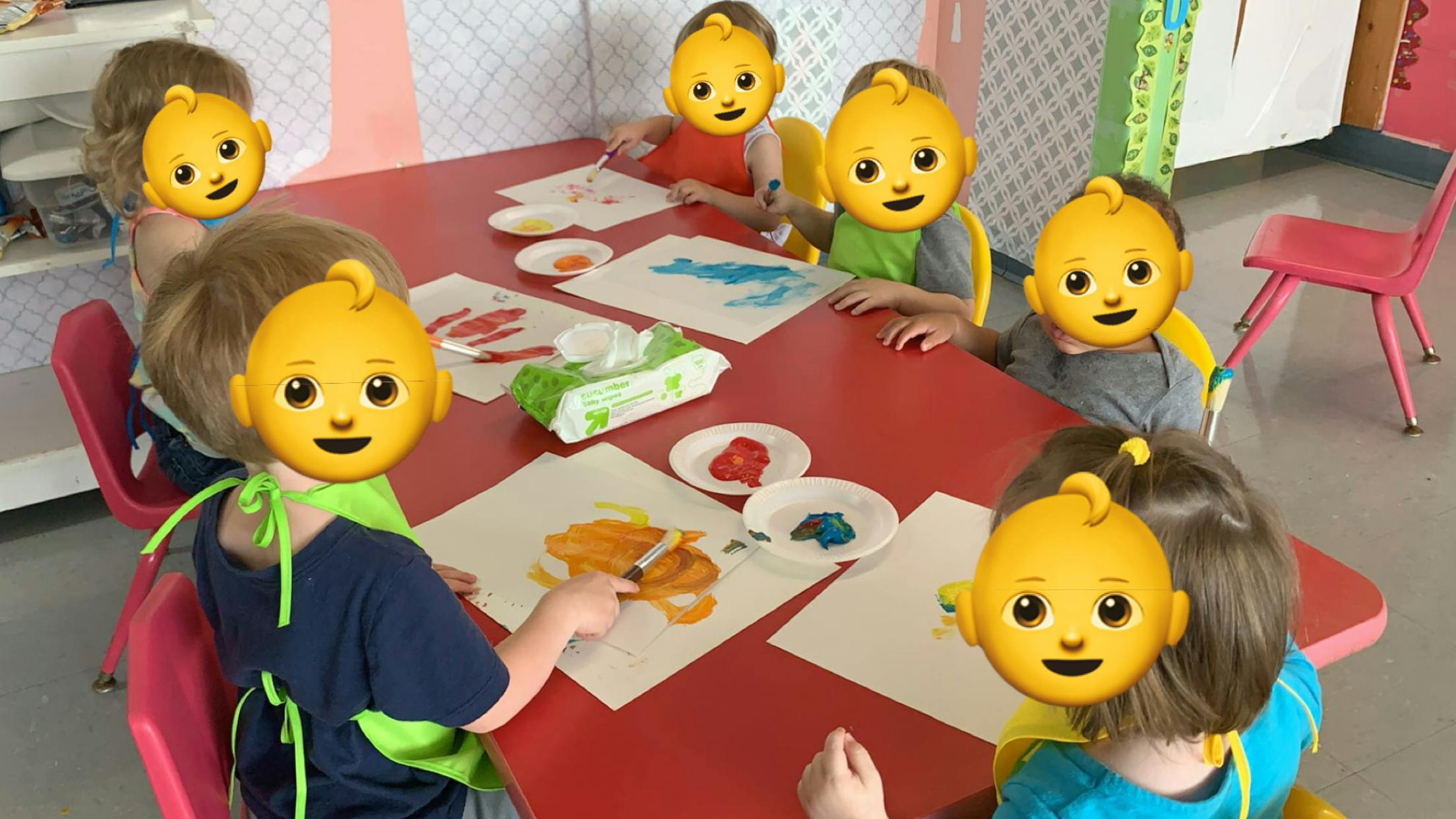 Children painting with brushes on paper at a red table
