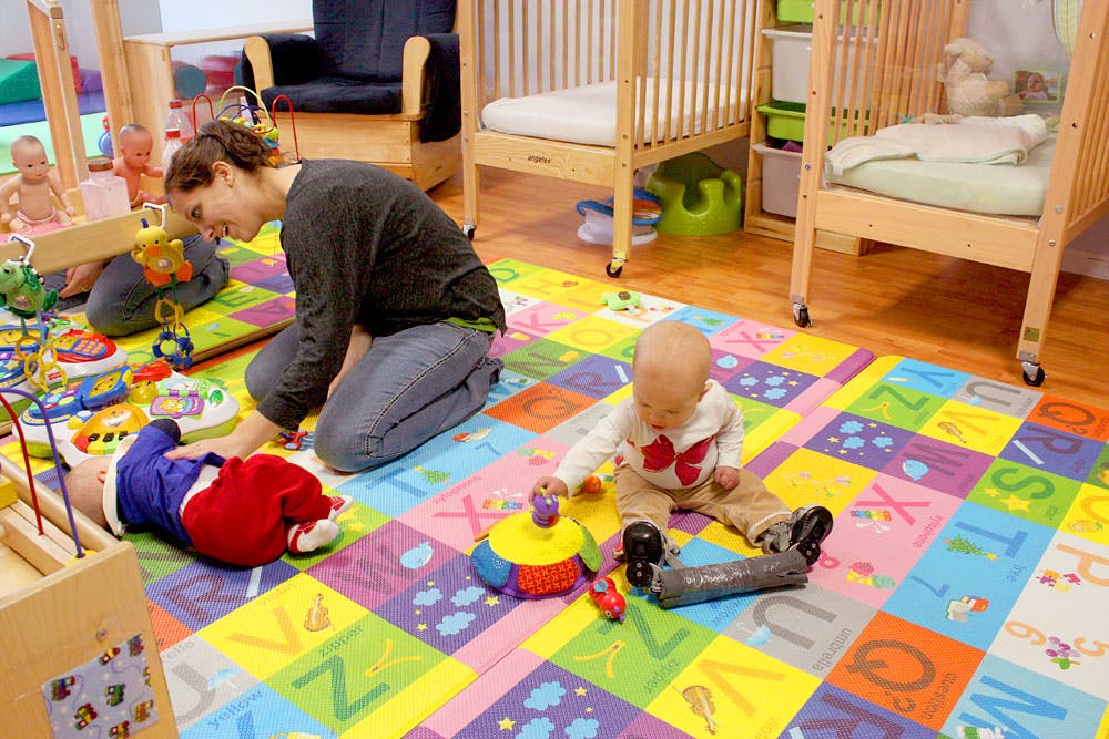 Person kneeling on a colorful mat with two babies and three children playing