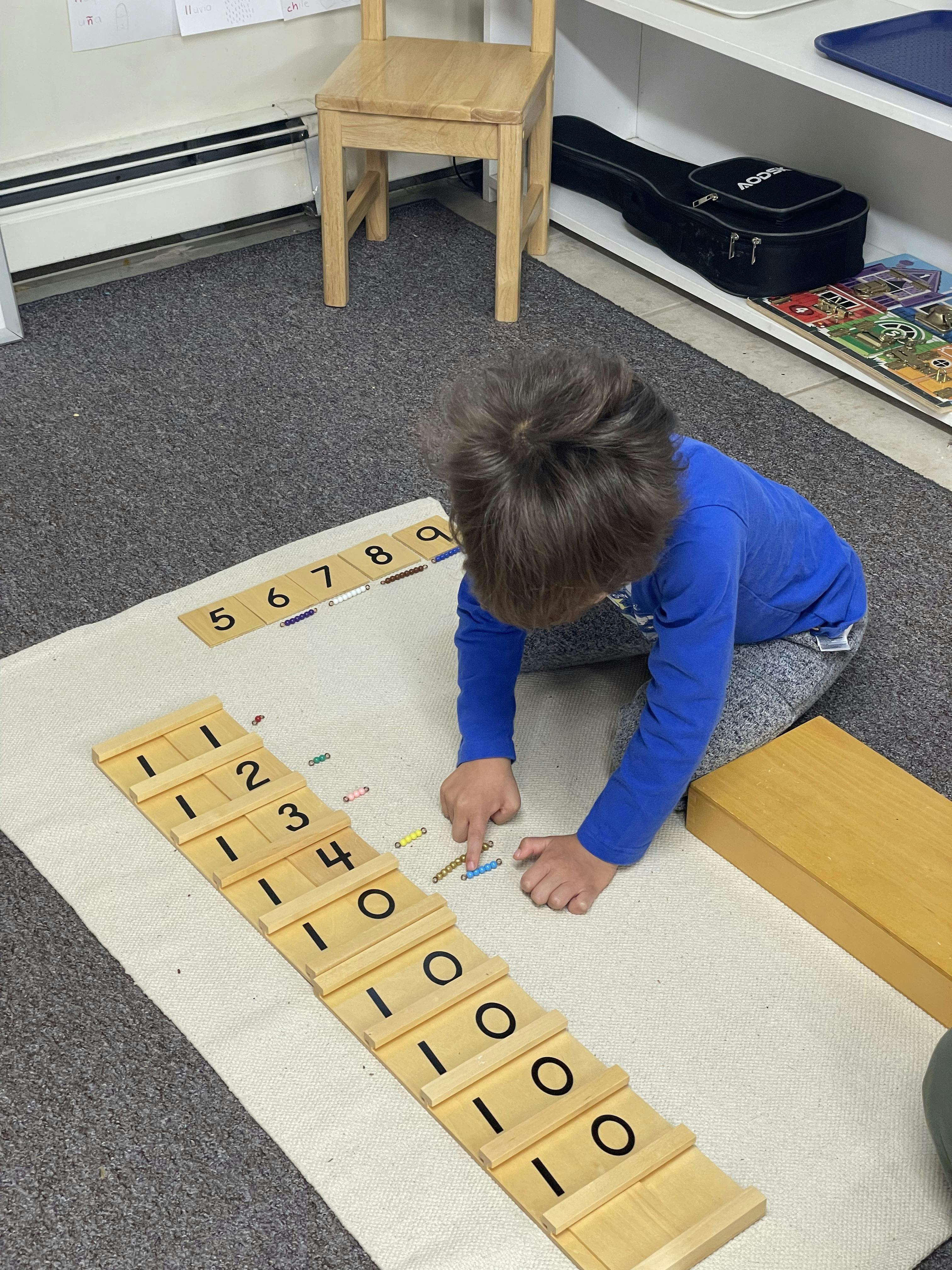 Child sitting on floor using Montessori number counting beads and tiles