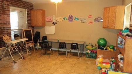 Empty classroom with small tables and chairs, high chair, and toys