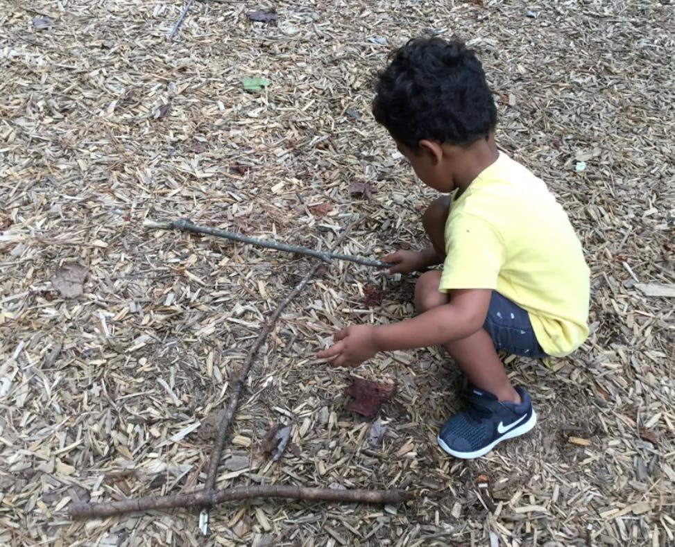 Child crouching on wood chips, holding a stick