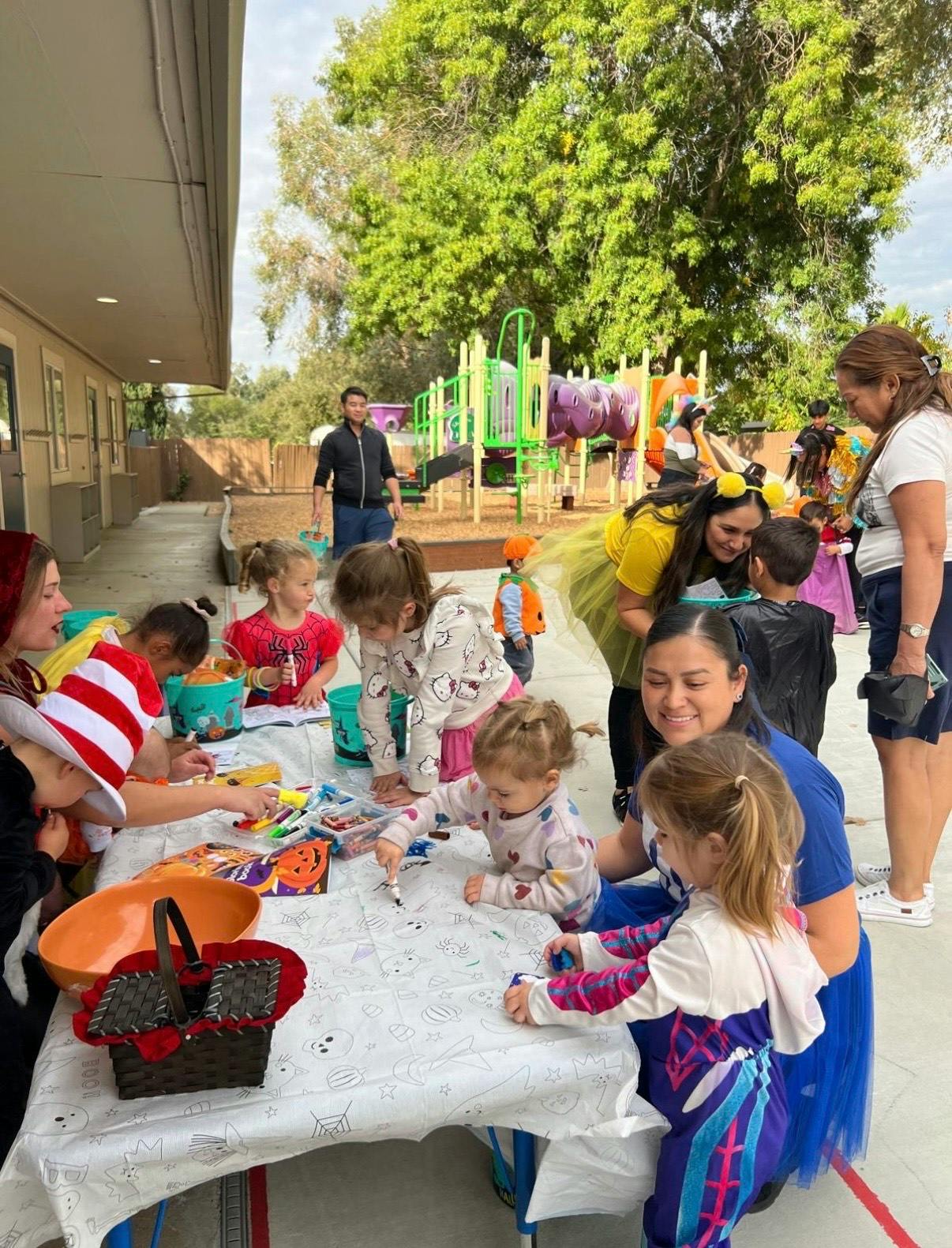 People and children gathered around a table with crafts on a playground
