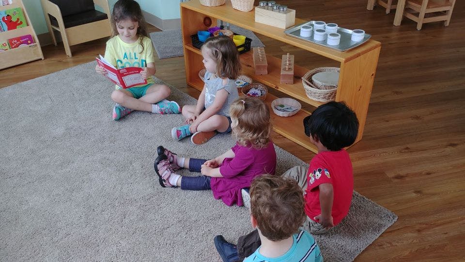 Child reading a book to other children sitting on a rug