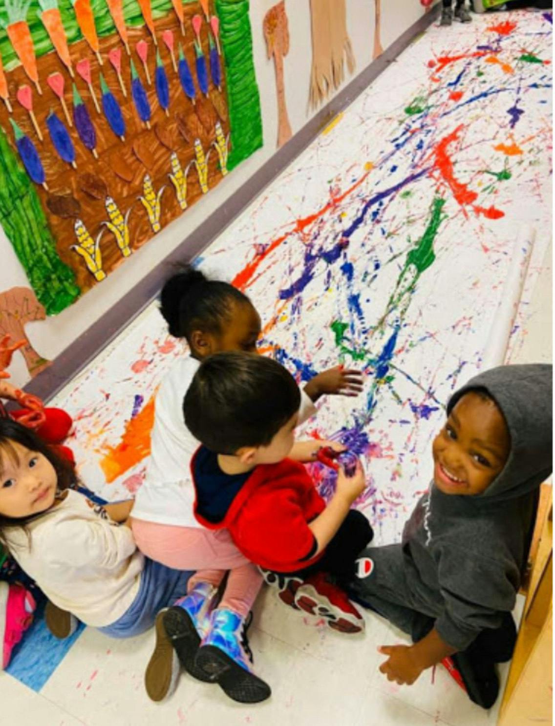 Children painting on a large sheet of paper on the floor