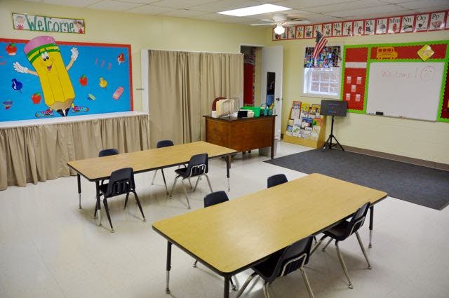 Empty classroom with tables and chairs, bulletin boards, and a whiteboard