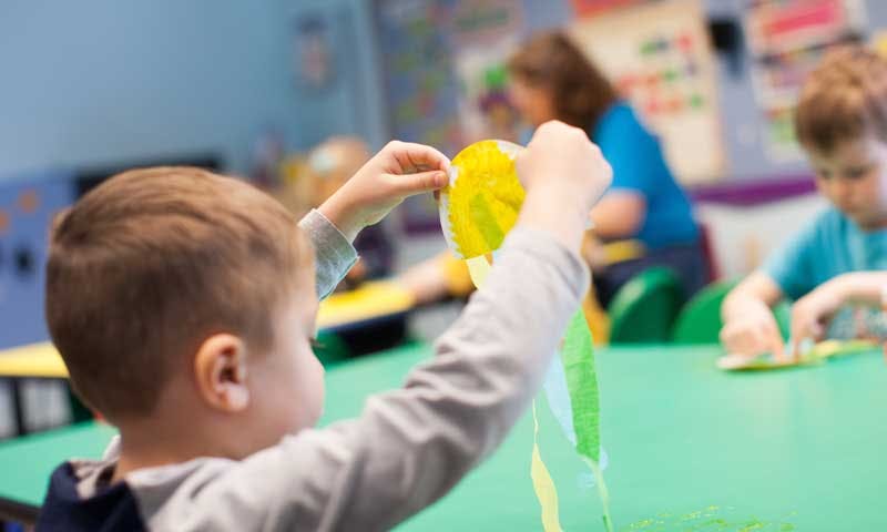 Child holding a yellow and green craft item in a classroom