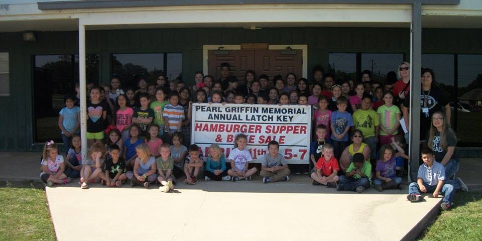 Large group of children and adults posing with a sign for a hamburger supper and bake sale