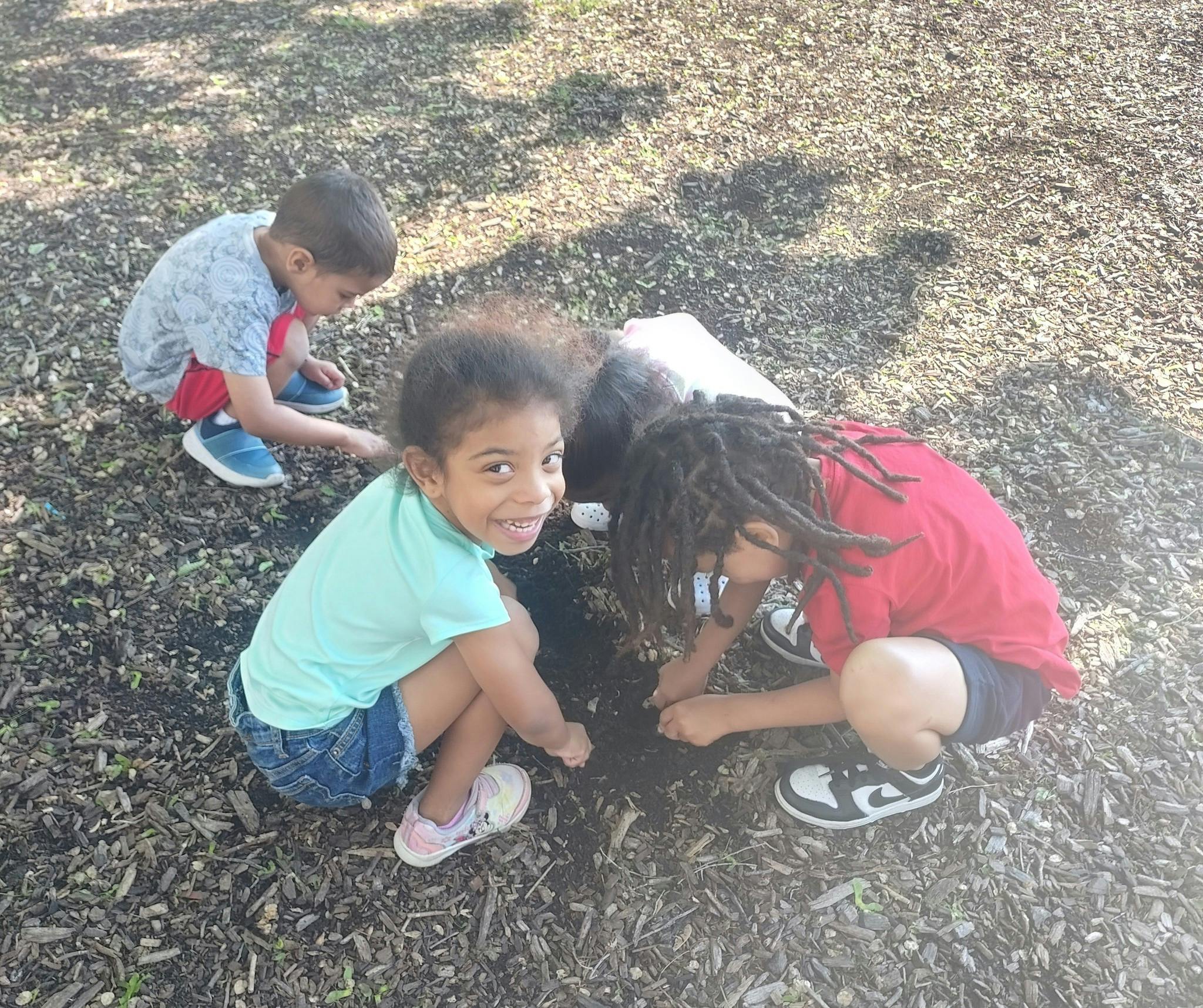 Three children crouching and digging in wood chips