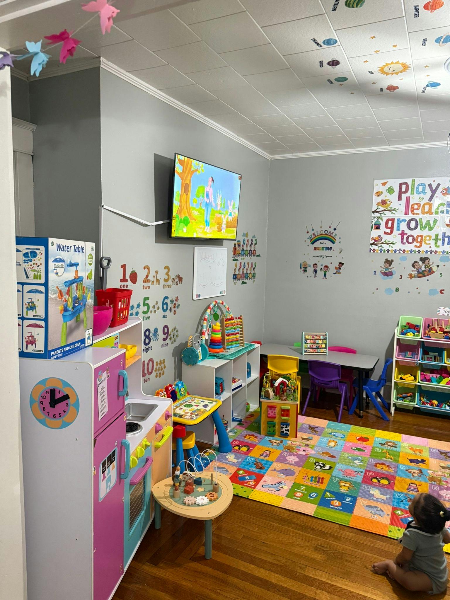 Child sitting on a colorful playmat in a playroom with toys and furniture
