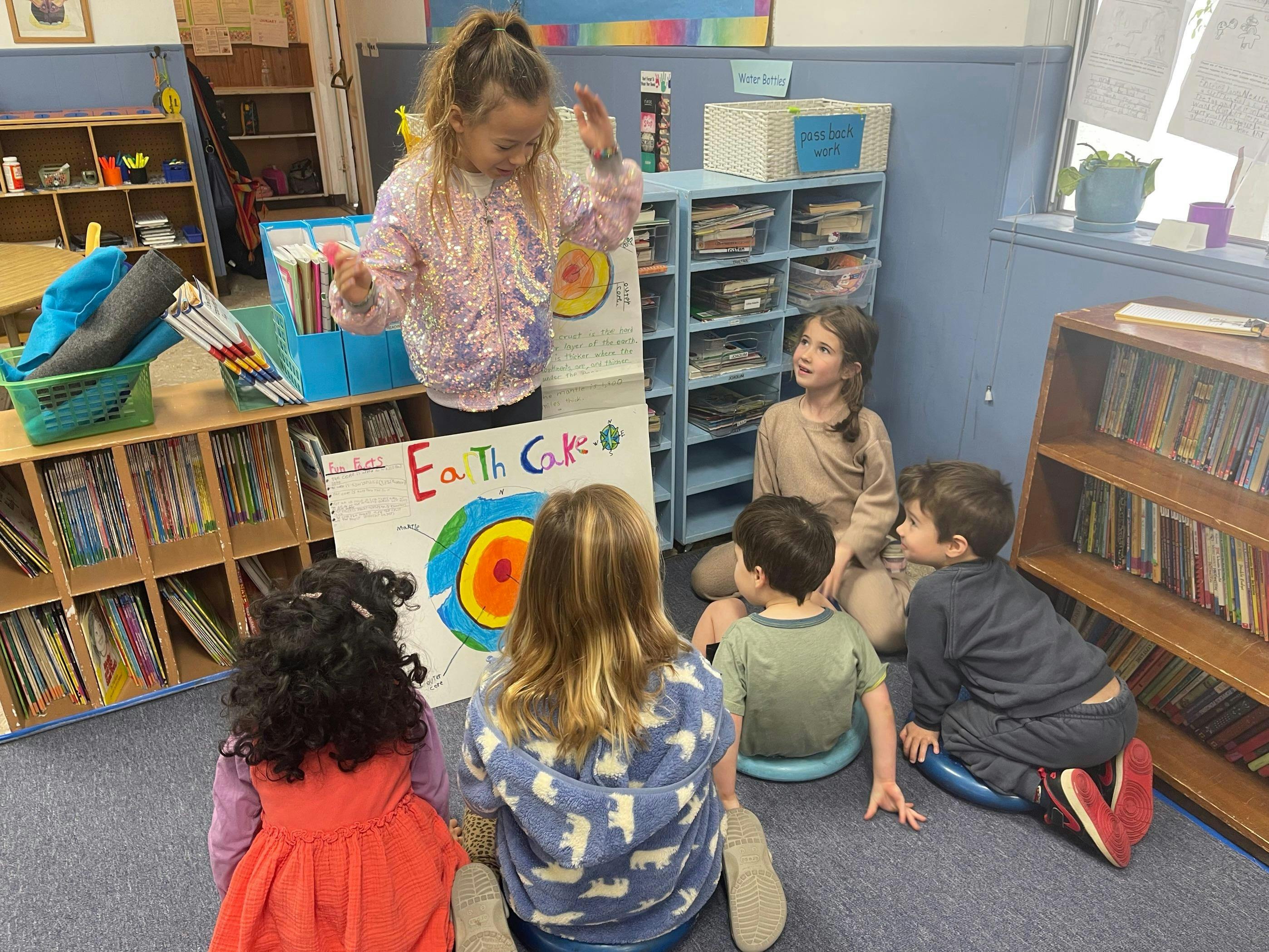 Child presenting a poster to other children sitting on the floor in a classroom