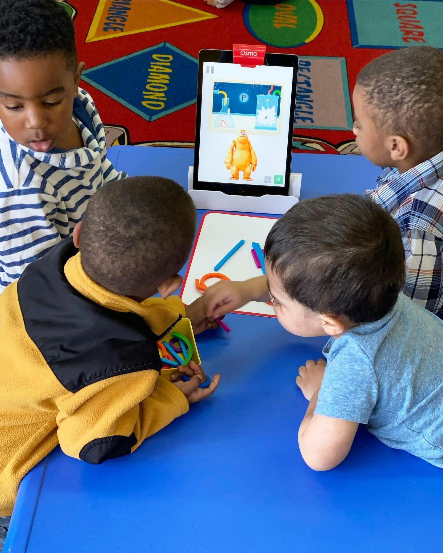 Three children at a table with a tablet and drawing materials