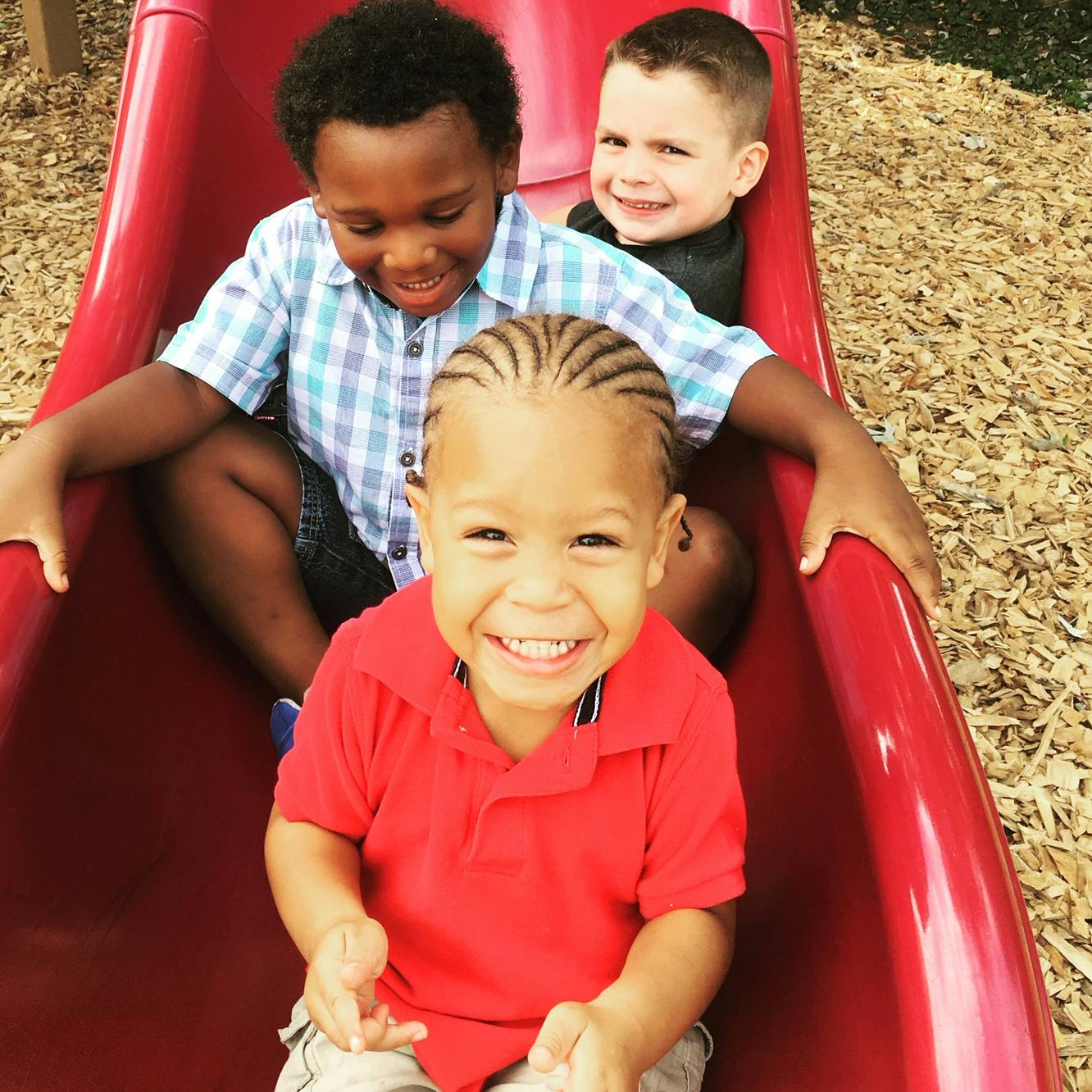 Three children sitting on a red slide
