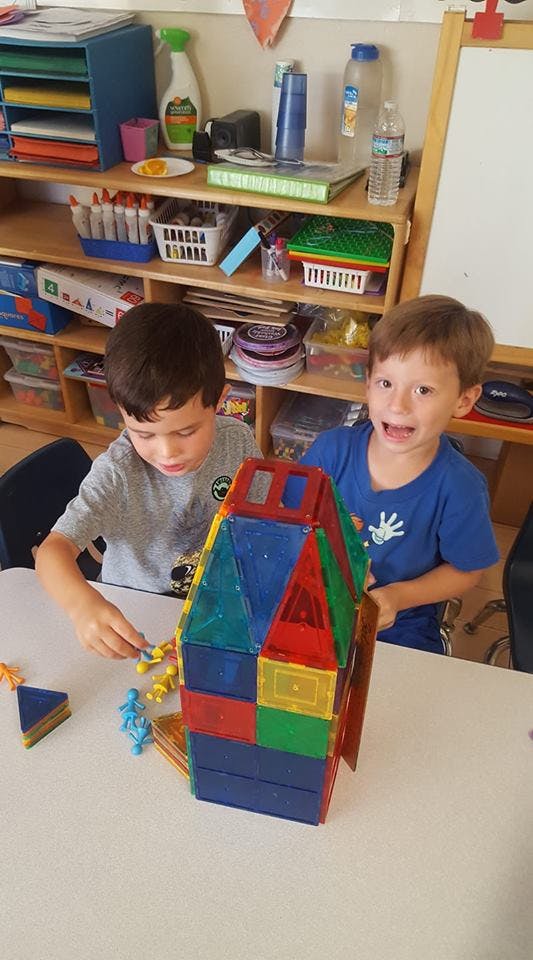 Two children playing with colorful magnetic building blocks in a classroom