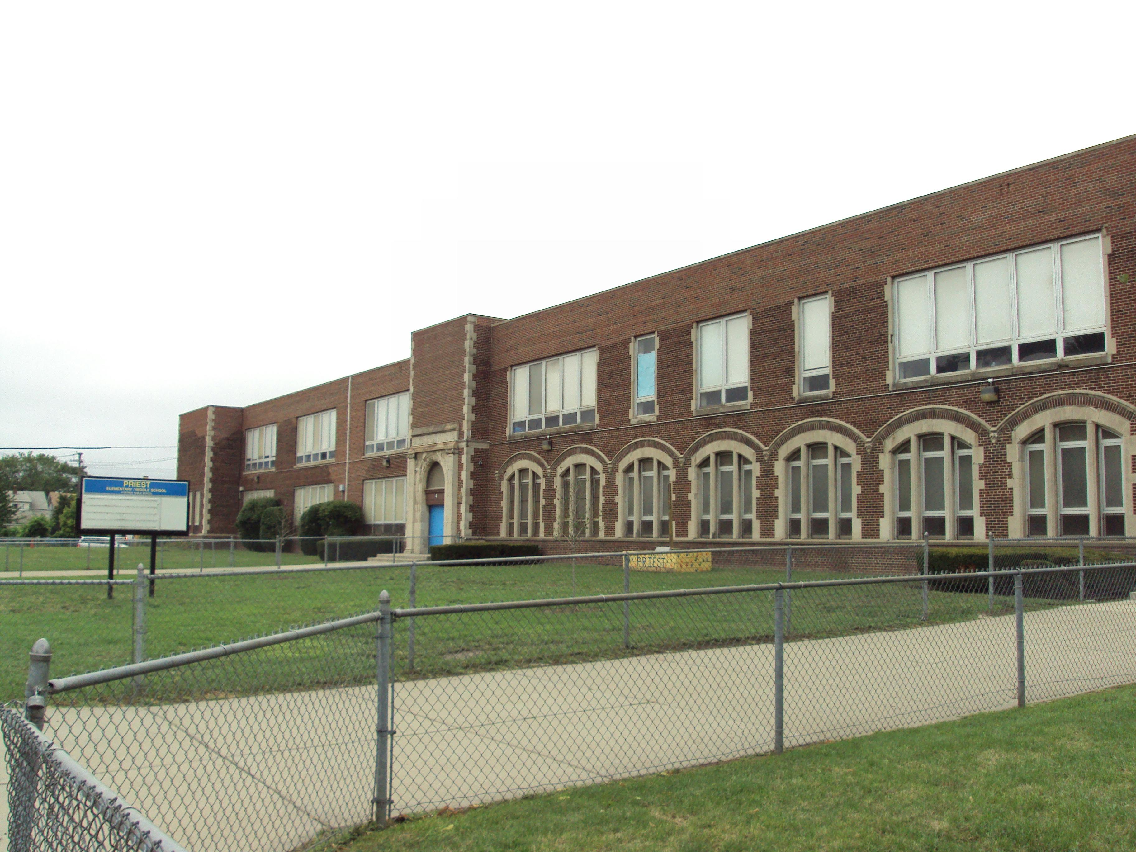 Brick school building with arched windows and a fence in the foreground