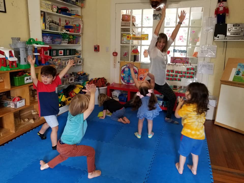 Adult and children with arms raised in a classroom