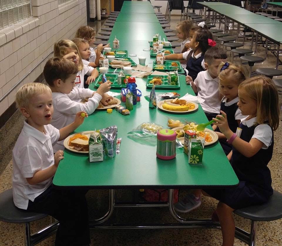 Children eating lunch at a long green table