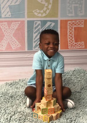 Child sitting on rug building a tower with blocks