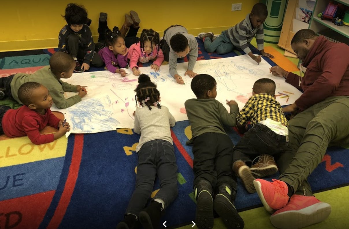 Adult and children drawing on a large sheet of paper on the floor