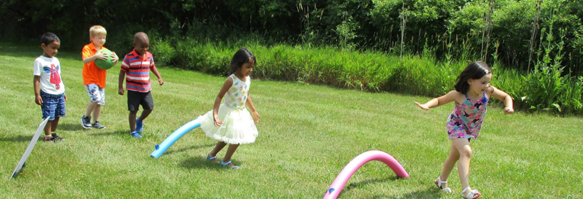 Children playing with pool noodles on a grassy field