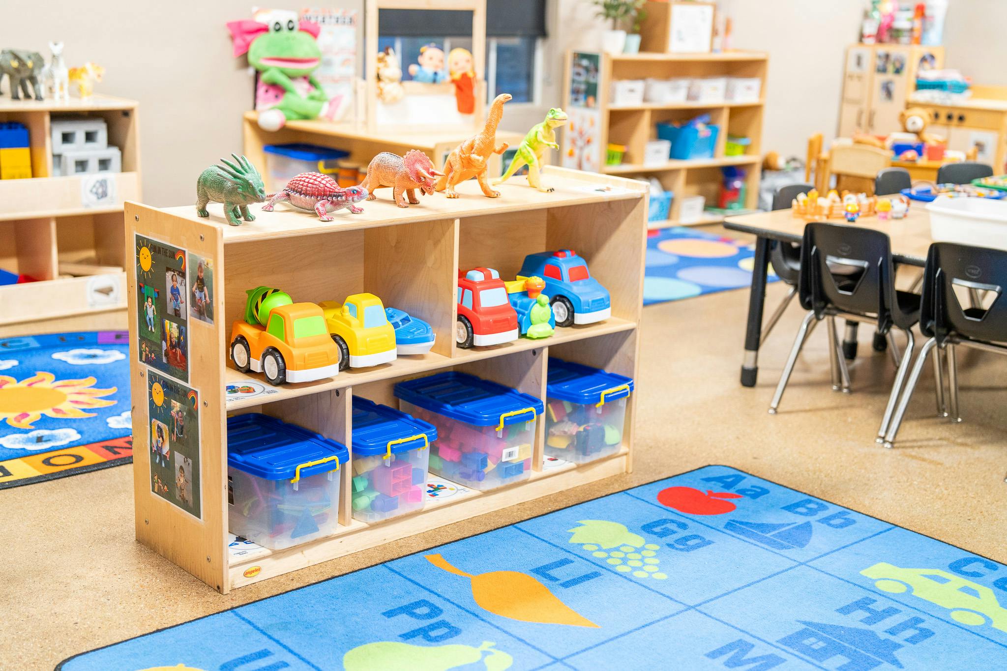 Dinosaur figurines and toy vehicles on wooden classroom shelves