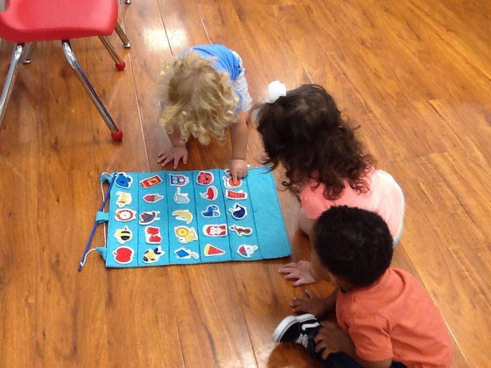 Three children on the floor looking at a blue mat with colorful shapes