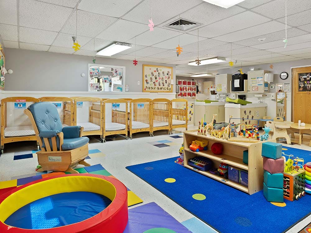 A nursery classroom with multiple cribs, a rocking chair, and play mats