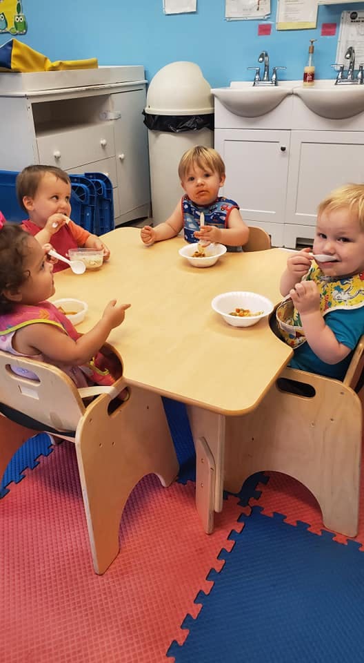 Four children eating at a small table in a classroom