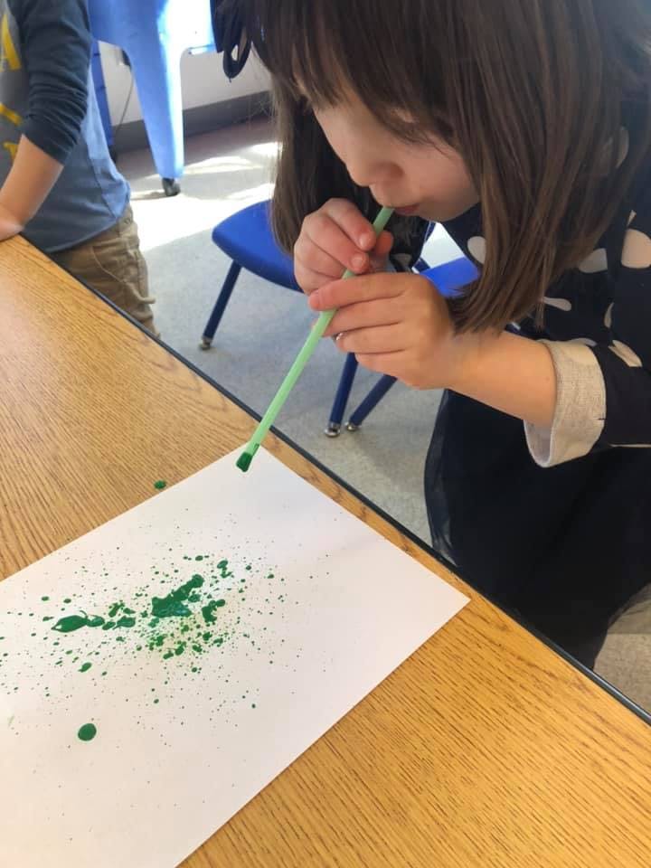Child blowing green paint through a straw onto paper