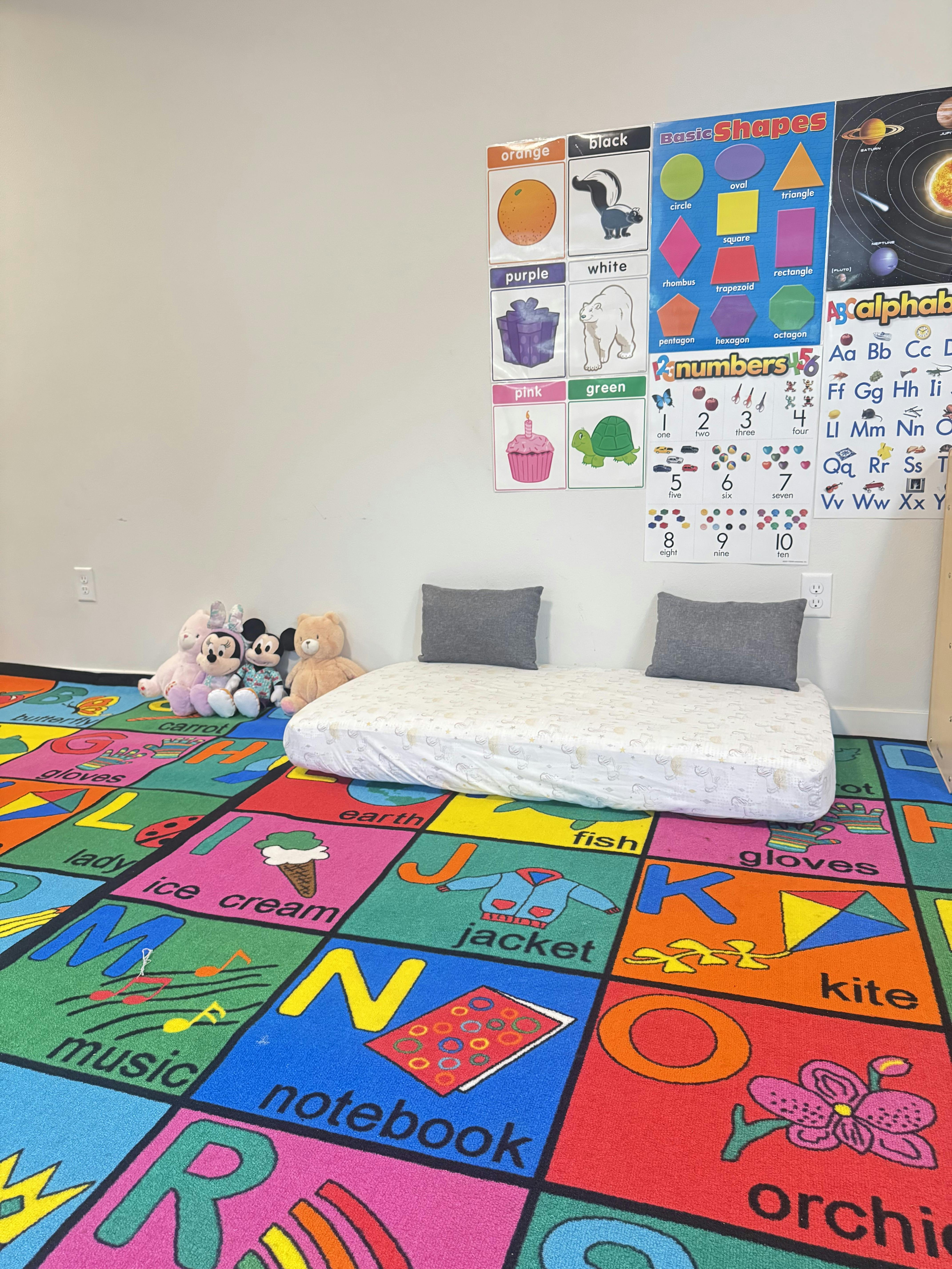 Small mattress on a colorful alphabet play rug with plush toys