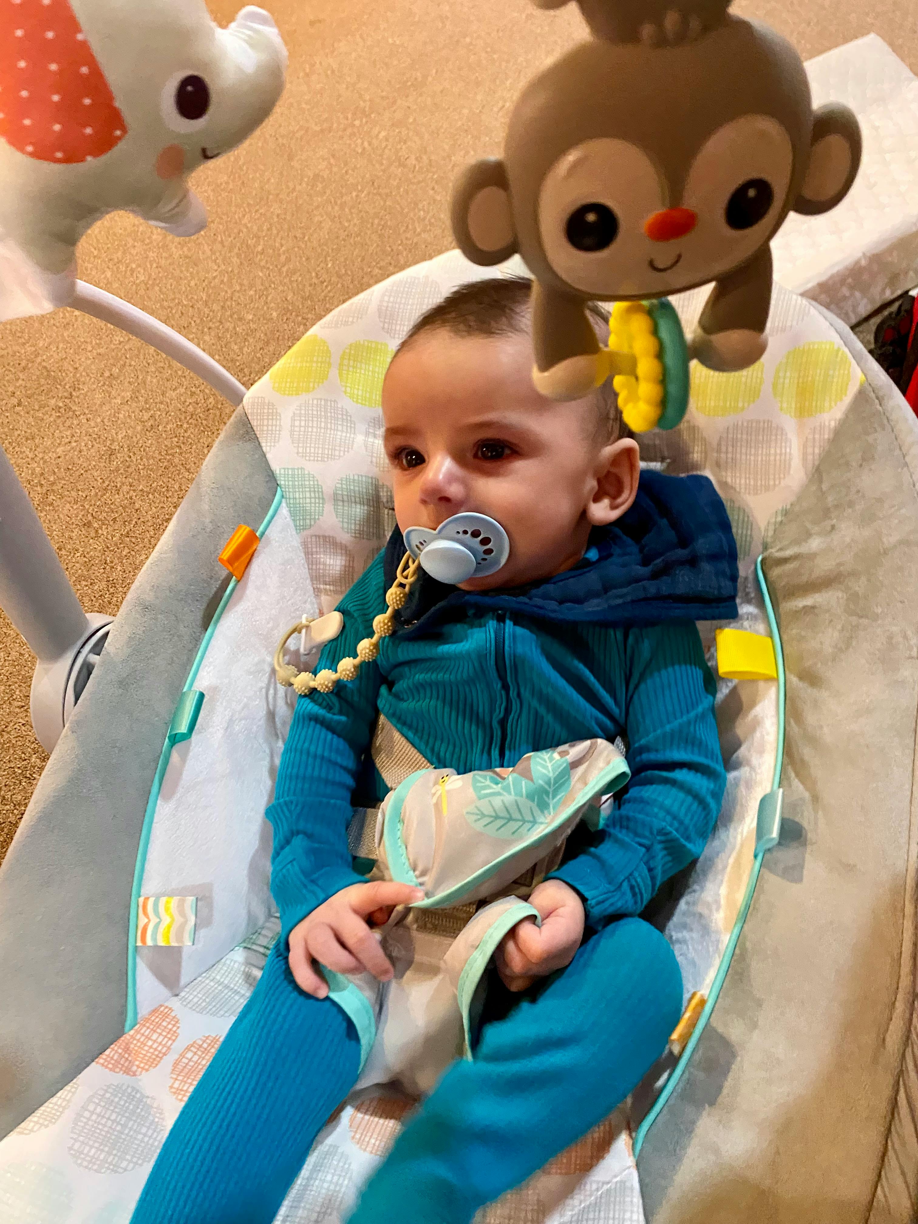 Child with pacifier in a baby bouncer with hanging toys