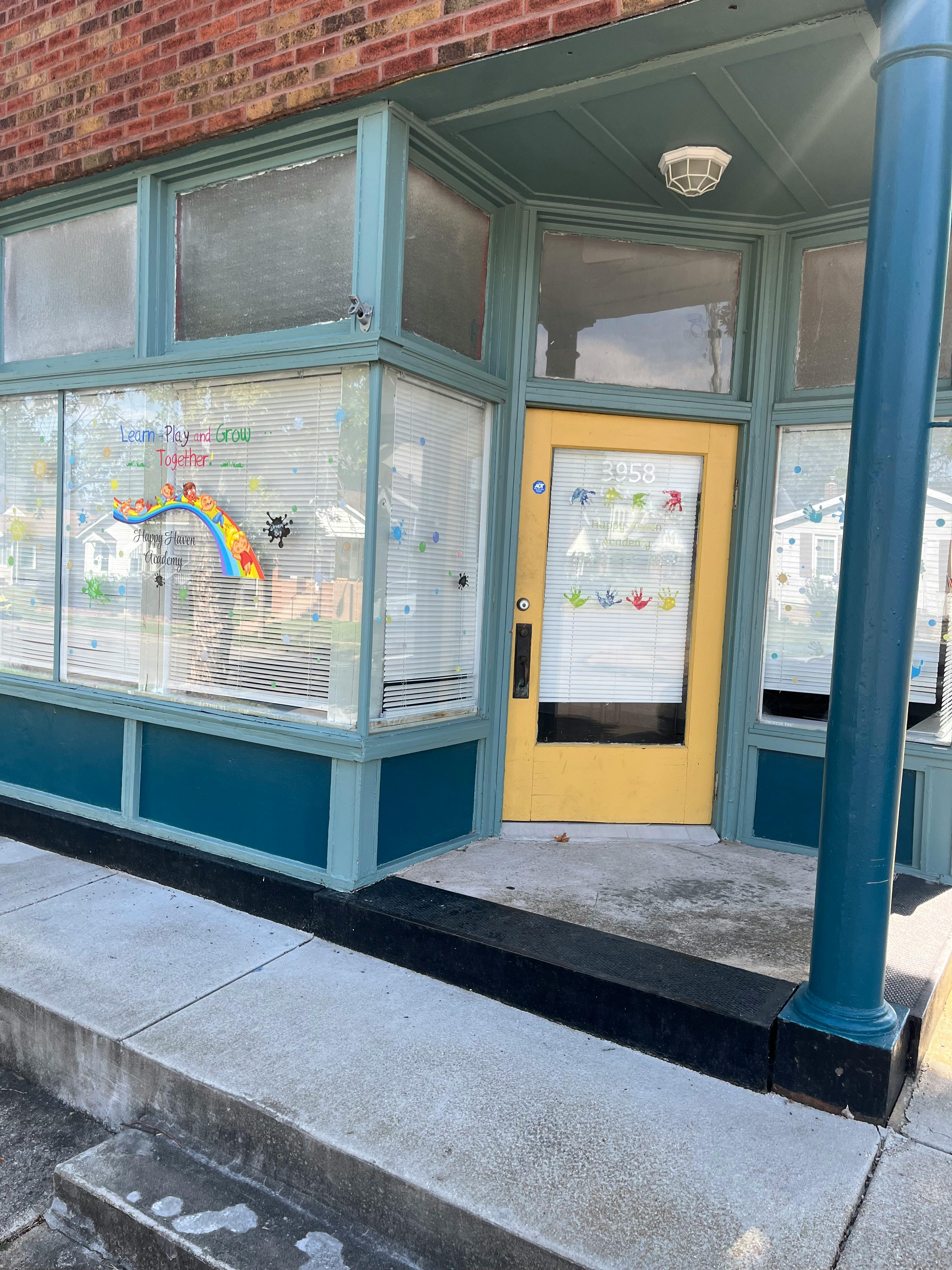 Storefront with a yellow door and windows decorated with children's art
