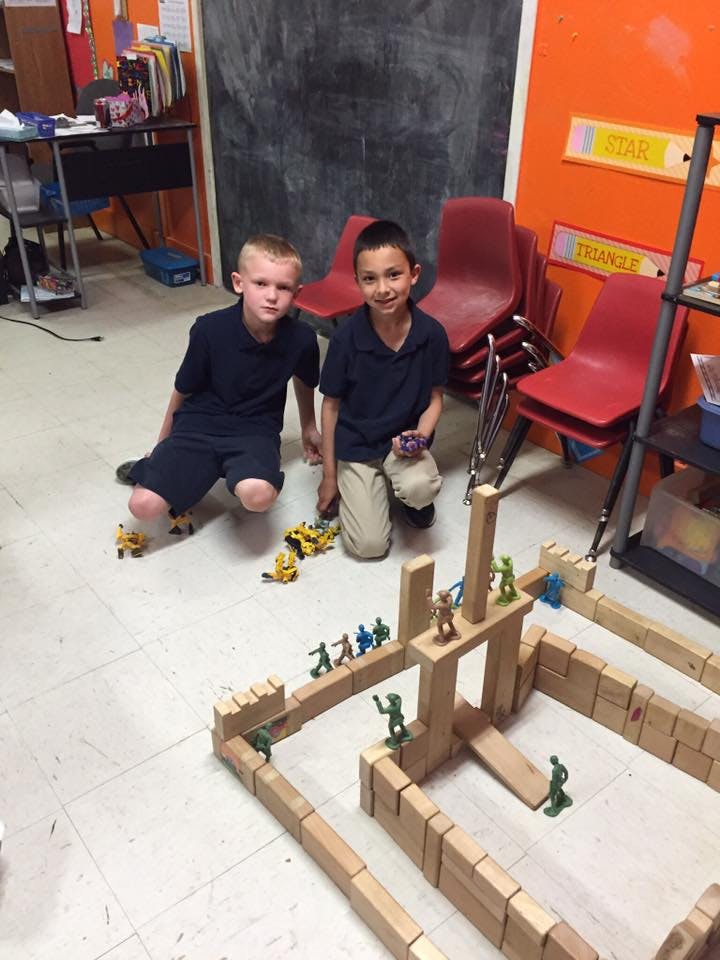 Two children playing with toy blocks and action figures on the floor