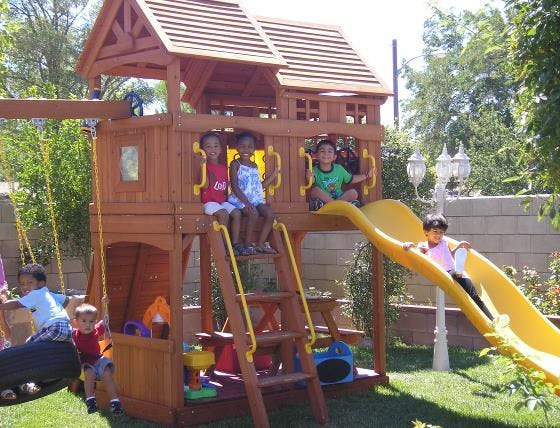 Children playing on a wooden playset with a slide and swings
