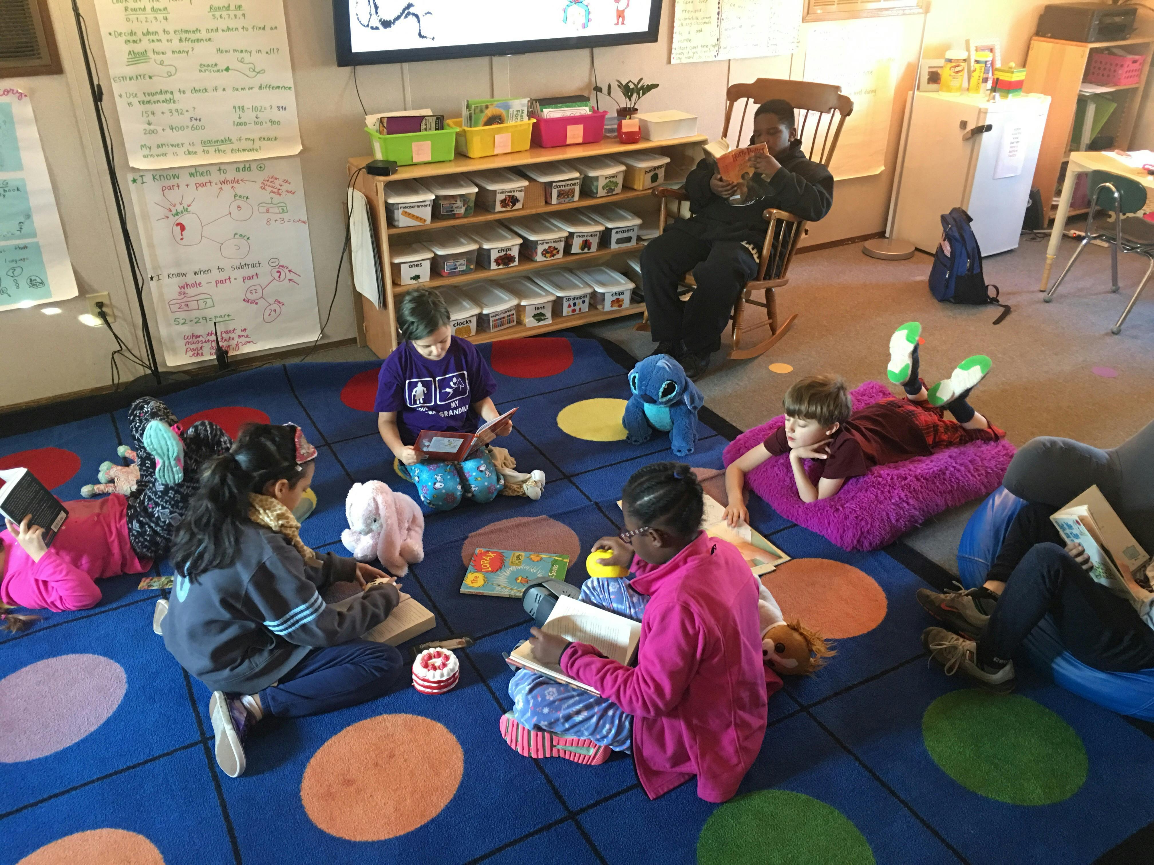 Children reading books on a colorful carpet in a classroom