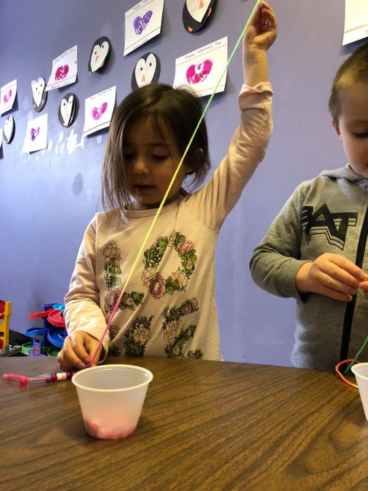 Child holding a string over a cup, another child in the background