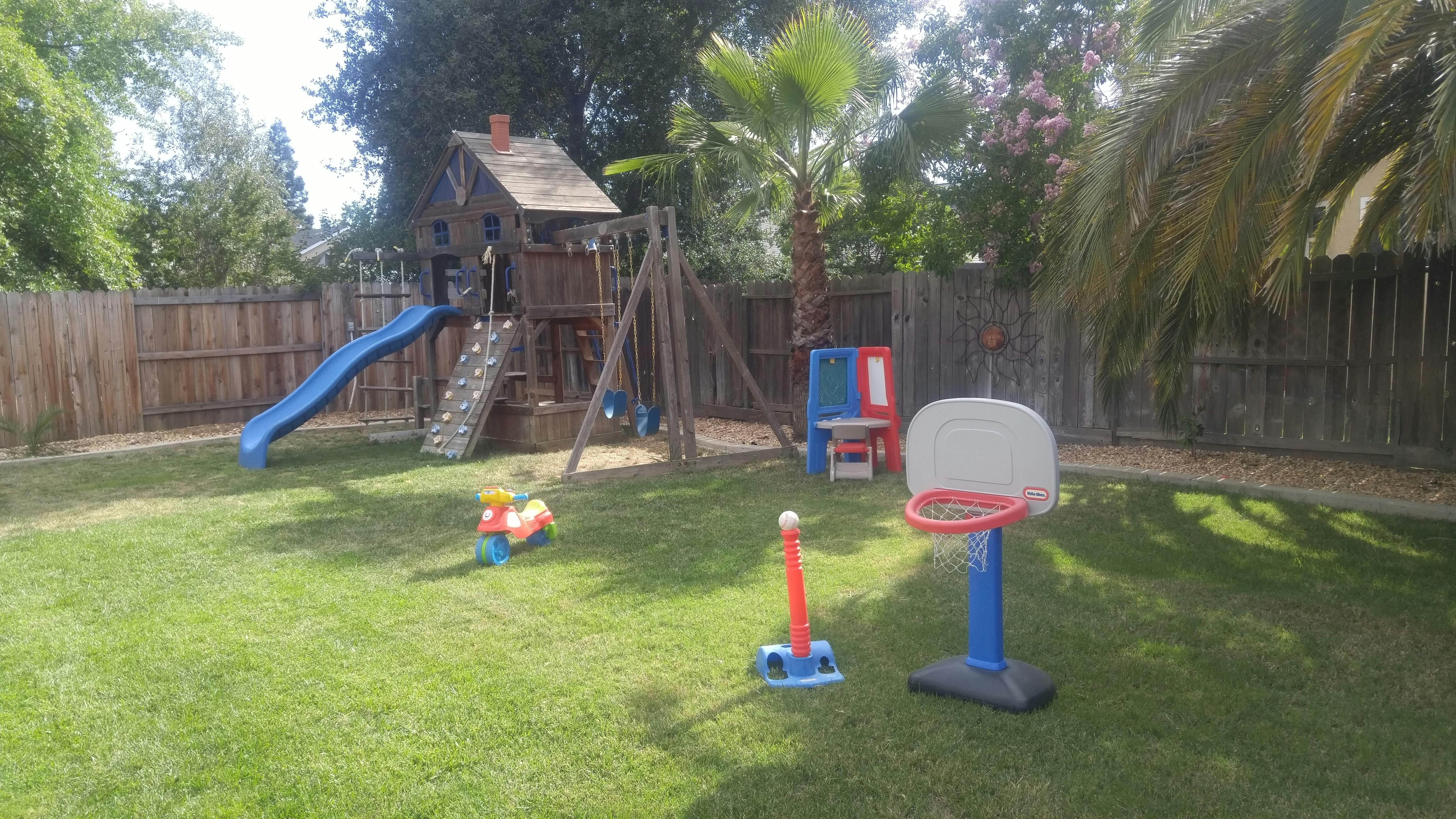 Backyard with a wooden play structure, blue slide, and basketball hoop