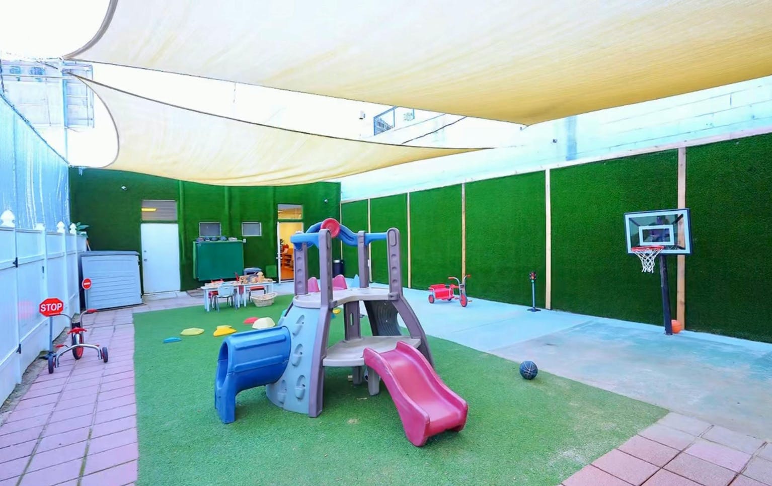 Playground with a slide and a basketball hoop under a shade canopy
