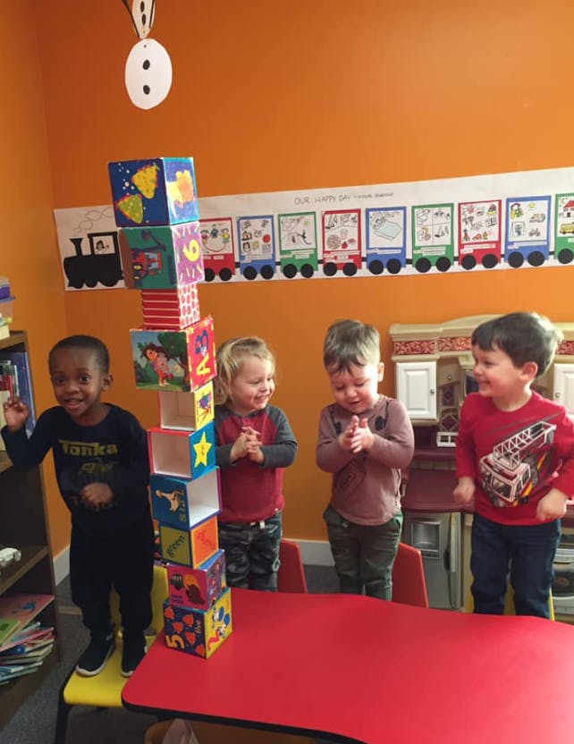 Three children standing around a tall stack of colorful blocks