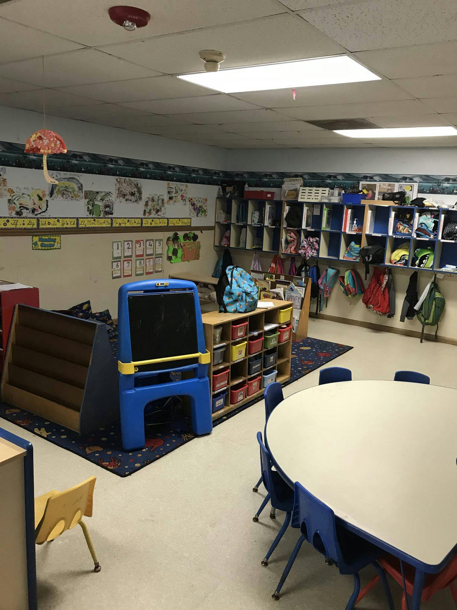 Classroom with a round table and chairs, storage shelves, and an easel