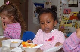 Child eating fruit from a bowl at a table
