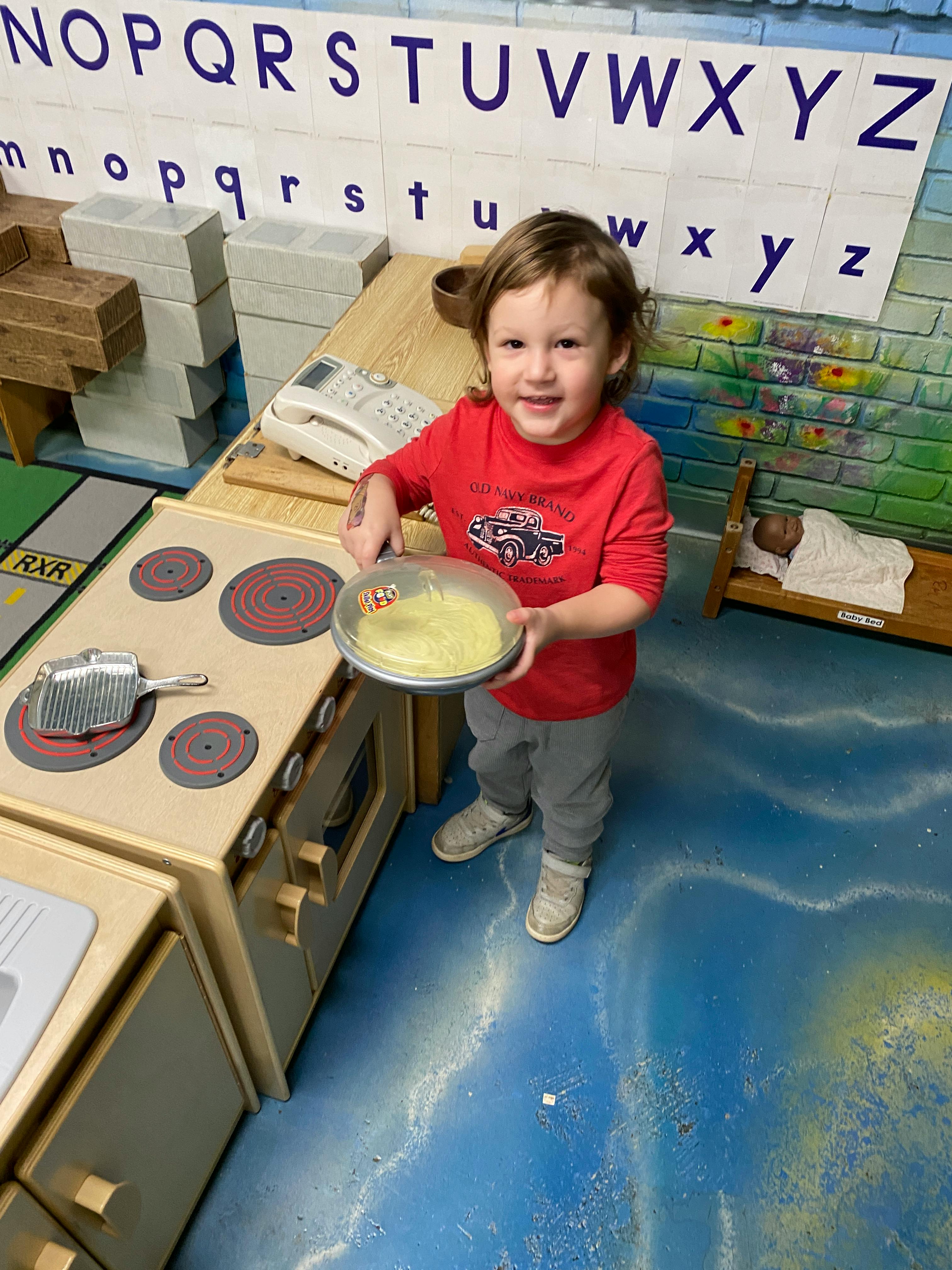Child holding a toy pan with food in a play kitchen
