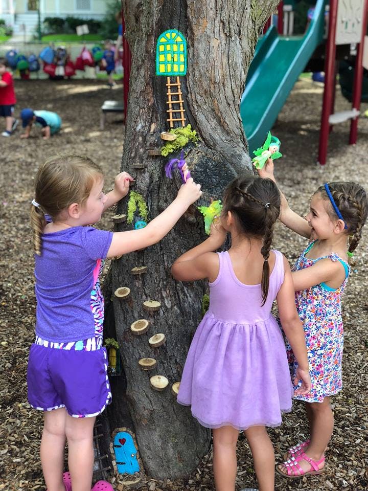 Three children playing with decorations on a tree trunk