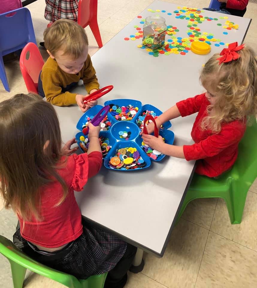 Three children playing with colorful sorting toys at a table