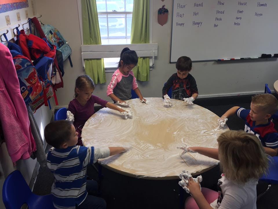 Children playing with shaving cream on a table in a classroom