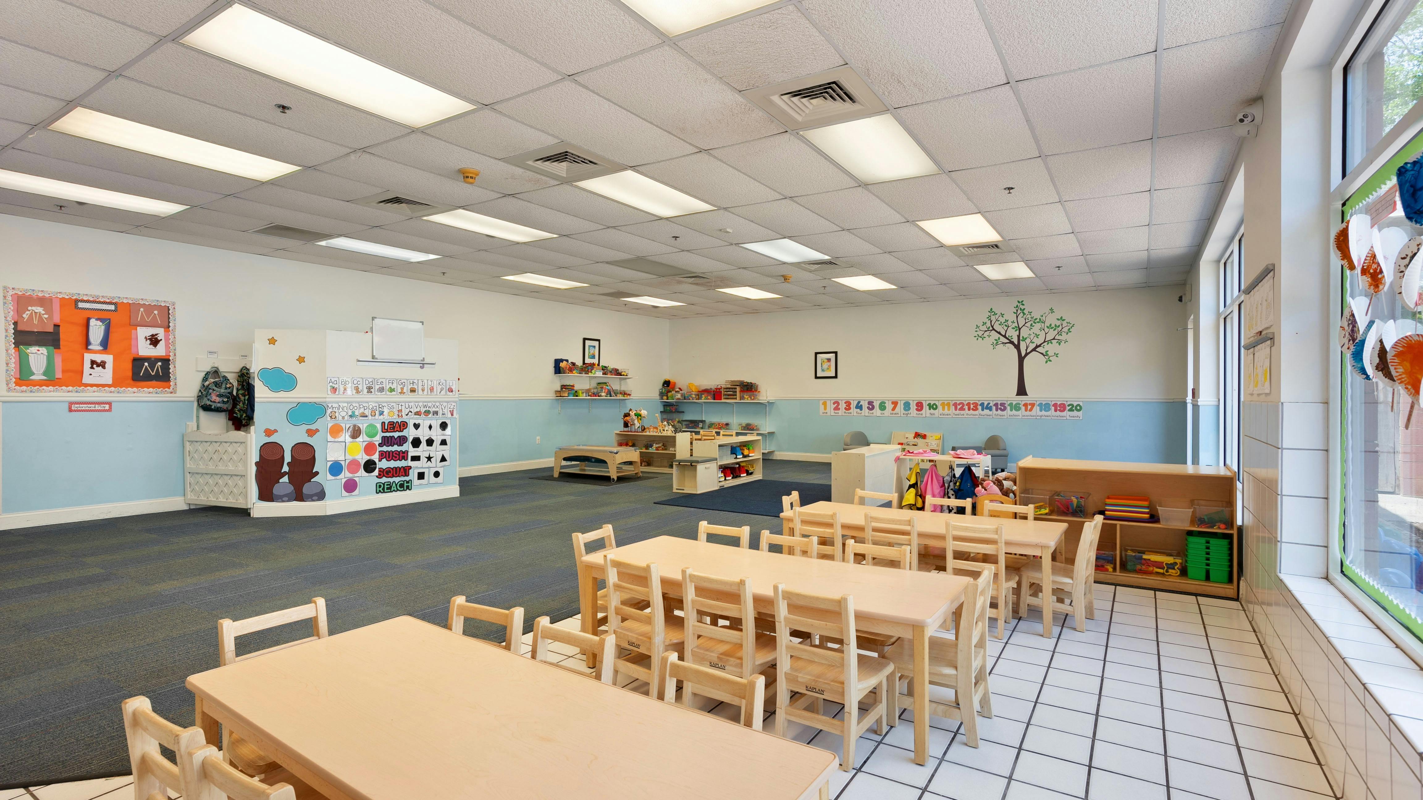 An empty early childhood classroom with small tables and chairs, shelves, and decorations