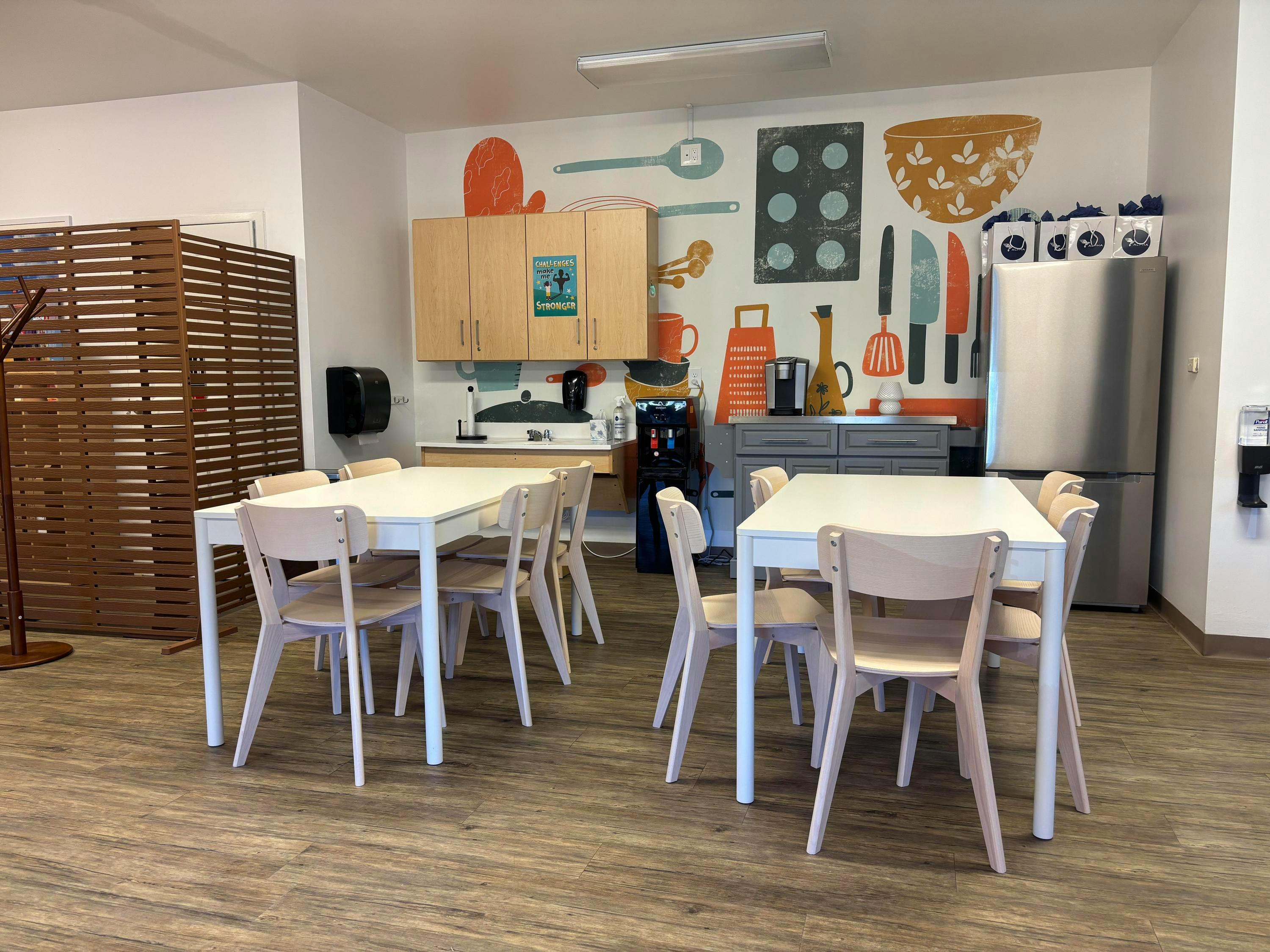Kitchenette with white tables and light wood chairs, wall mural of kitchen items