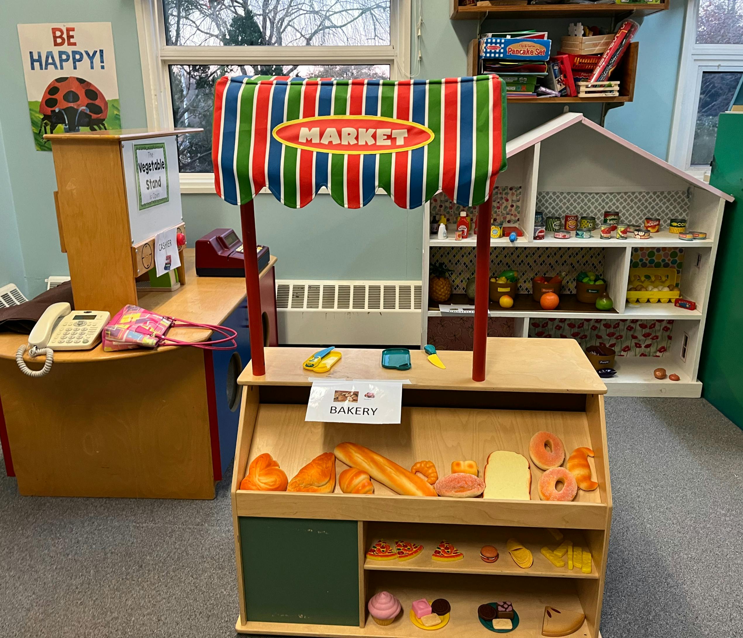 A play market stand with a striped awning and "MARKET" sign, next to a dollhouse