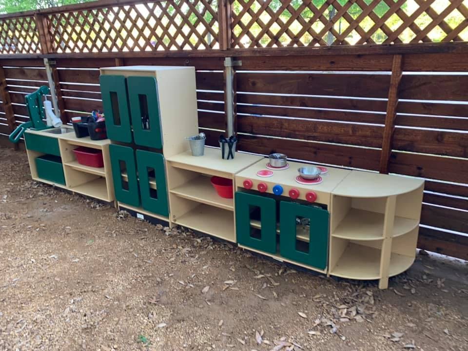 Outdoor play kitchen set with green cabinets and wooden shelves