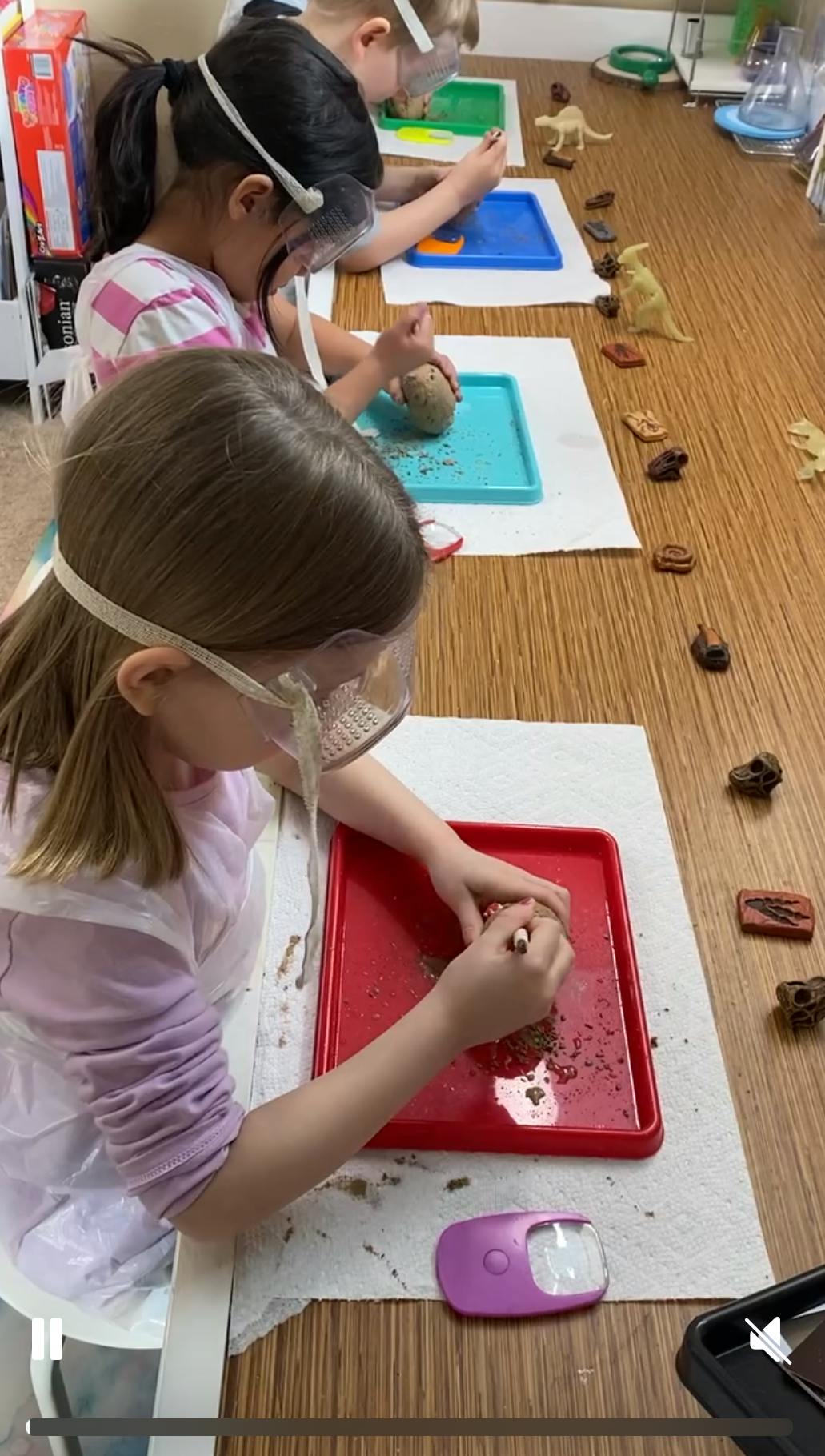 Children wearing safety goggles excavating objects from clay on trays