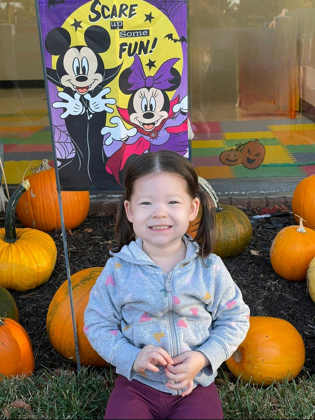 Child sitting in front of pumpkins and a Halloween banner